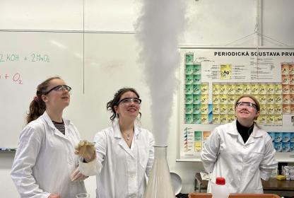 Studentky v laboratorních pláštích sledují pokus, ze kterého stoupá bílý dým