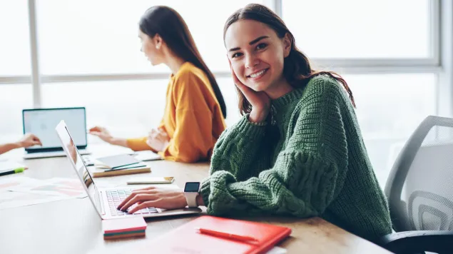 Usměvavá studentka u notebooku ve světlé učebně